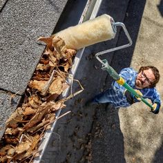 a man holding a paint roller next to a pile of leaves on the side of a road