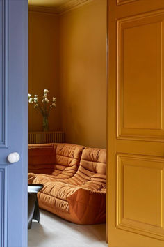 an orange couch sitting in front of a blue door next to a vase with flowers