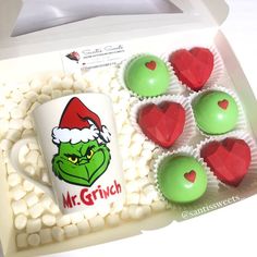 the grin face coffee mug is next to some green and red heart shaped cupcakes