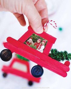 a hand holding a red toy car with christmas decorations on it's side and a small tree in the back