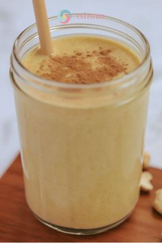 a glass filled with some kind of drink on top of a wooden table next to nuts