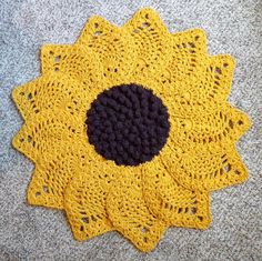 a yellow crocheted doily with a black center sits on the floor next to a gray carpet