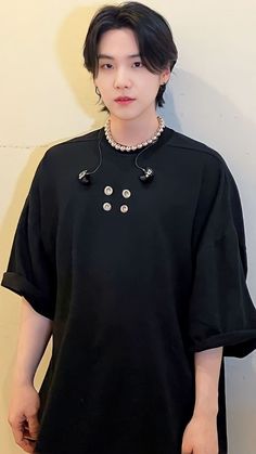 a young man standing next to a white wall wearing a black shirt with buttons on it