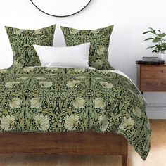 a bed with a green and white comforter on it next to a wooden dresser