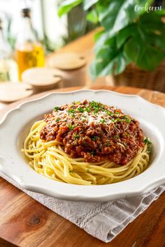 a plate of spaghetti with sauce and parmesan cheese on the side sitting on a wooden table