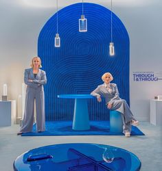 two women sitting on blue stools in an exhibit