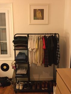 a rack with clothes and shoes on it in a room next to a dresser or window