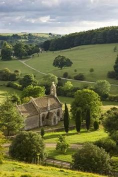 an old church in the middle of a lush green field with trees on both sides