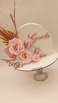 a white cake topped with pink flowers and gold leaf decorations on top of a metal stand