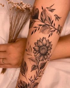 a woman's arm with flowers and birds tattoo on her left arm, while holding a dried flower