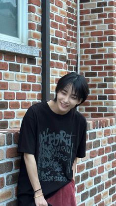 a young man leaning against a brick wall