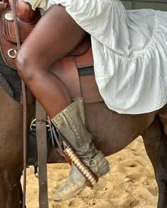 a woman sitting on the back of a brown horse wearing cowboy boots and a white dress