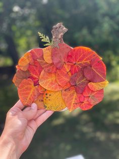 a person holding up a small piece of paper with leaves in the shape of a pumpkin