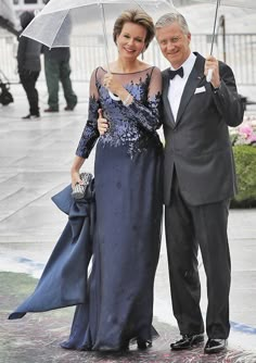 a man and woman standing under an umbrella in the rain, dressed in formal wear