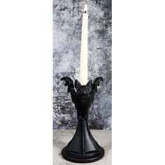 a black candle holder with a white candle in the shape of a bat on it