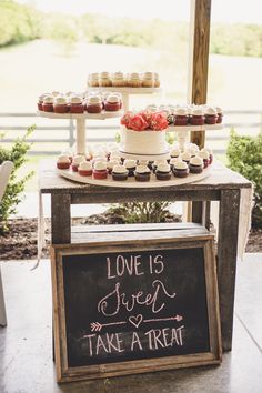 a table topped with cupcakes next to a chalkboard that says love is sweet take a treat