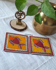 two coasters sitting on top of a table next to a vase with a plant