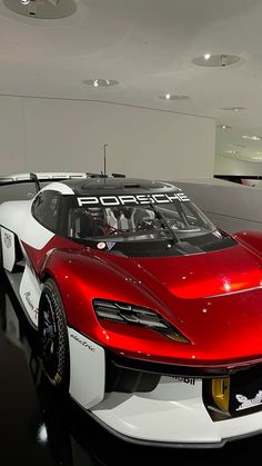 a red and white sports car on display in a showroom with people looking at it