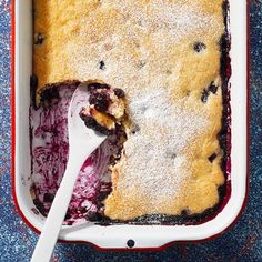 a blueberry cobbler in a red and white dish with a spoon sticking out of it