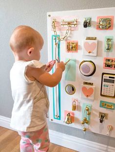 a baby standing in front of a bulletin board with lots of magnets on it