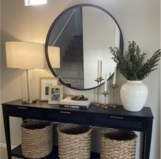 a black table with baskets and a round mirror on it next to a vase filled with flowers