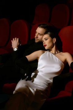 a man and woman in formal wear sitting next to each other on a red chair