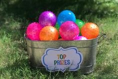 a metal bucket filled with lots of colorful balls on top of green grass in front of trees