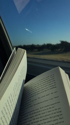 an open book sitting on top of a car seat next to a window in front of a blue sky