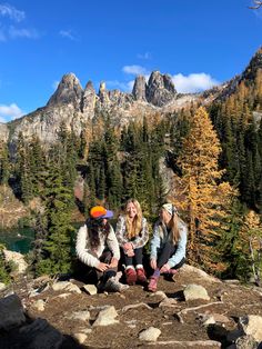 two women sitting on rocks in front of some trees and mountains with their feet crossed