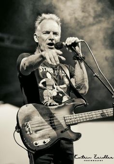 a man holding a guitar while standing next to a microphone on top of a stage