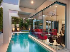 an indoor swimming pool with red chairs and tables next to the glass walled wall that surrounds it