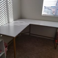 a corner desk in the corner of a room with shutters on the windowsill