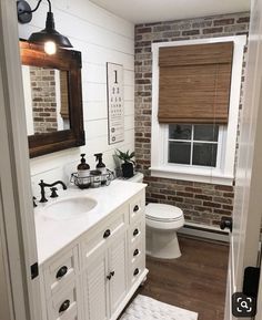 a white bathroom with brick walls and wood flooring is seen in the mirror above the sink