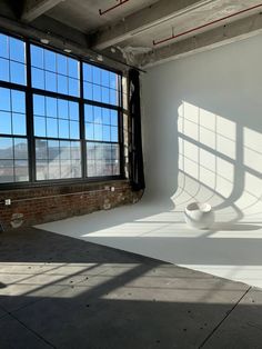 an empty room with large windows and a white bowl on the floor in front of it