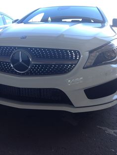 the front end of a white car parked in a parking lot next to other cars