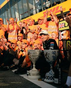 a group of men standing next to each other in front of a yellow bus holding up their hands