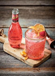 a pink drink with orange slices and a bottle on a cutting board next to it