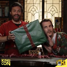 two men are holding presents in front of them and one is pointing at the camera