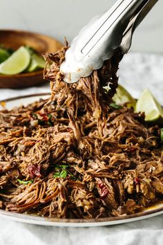 shredded meat being served on a plate with lime wedges