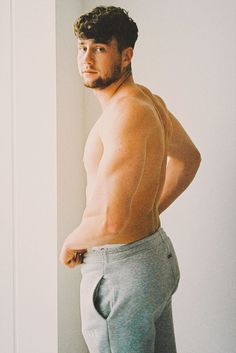 a shirtless man standing in front of a white wall with his hands on his hips