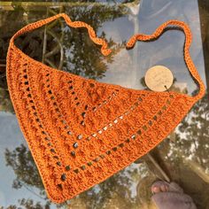 an orange crocheted purse hanging from a glass window with a coin in it