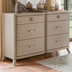 a dresser with two mirrors and vases on it's top, in front of a window