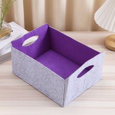 a gray and purple box sitting on top of a wooden table next to a lamp