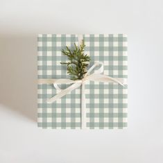 a present wrapped in plaid paper with a white ribbon tied around it and a sprig of pine on top