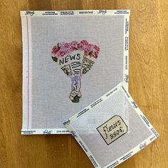 two cross - stitch cards are sitting next to each other on a wooden surface,