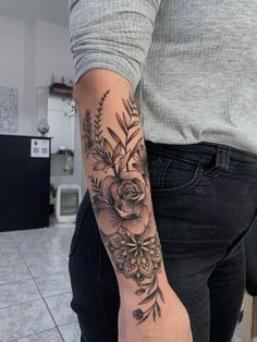 a woman's arm with flowers and leaves tattooed on her left arm, in black ink