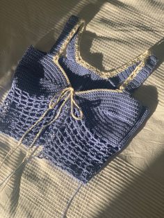 a blue crocheted bag sitting on top of a white bed sheet with a string attached to it