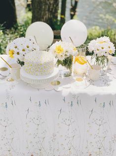 a table topped with a cake covered in white frosting next to flowers and balloons