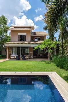 a pool in front of a house with grass and palm trees around the pool area