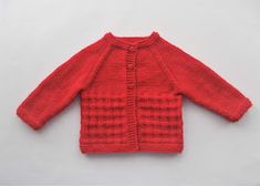 a red knitted cardigan sweater sitting on top of a white surface